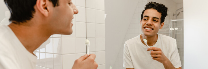 Smiling young hispanic man brushing teeth