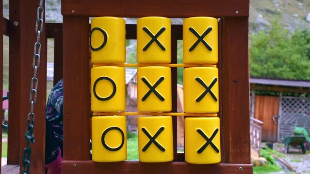 Tic Tac Toe game on playground equipment in the park. girl plays tic-tac-toe. Tic-tac-toe on the playground. The girl rotates cylinders with crosses.