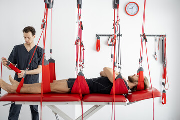 Rehabilitation specialist preparing for an active treatment on suspension straps with a male...