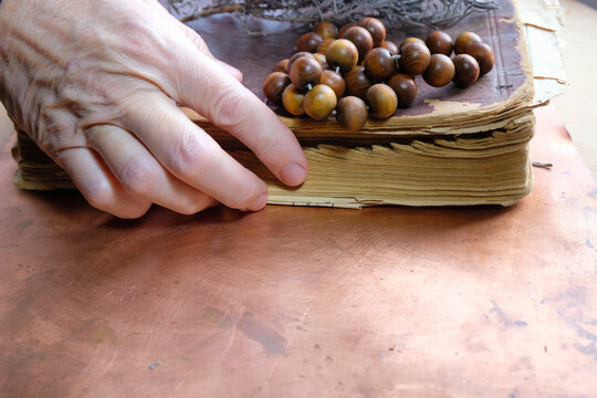 Old woman's hand takes an ancient book or Bible. There is a rosary on the book. Copy space. - Powered by Adobe