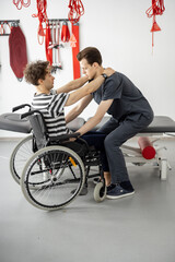 Rehabilitation specialist helps man to get up from a wheelchair at clinic. Concept of medical care...