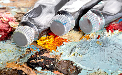 A wooden palette covered with old dried oil paints and tubes of oil paint.Top view. Close-up