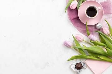Bouquet of pink spring tulip flowers, cup of coffee, chocolates and a greeting card on a white...