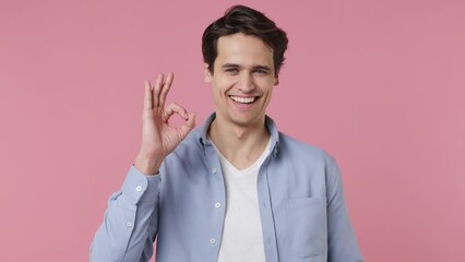 Smiling cheerful young brunet man 20s years old wears blue shirt look camera showing okay ok zero fingers gesture isolated on plain pink background studio portrait. People emotions lifestyle concept