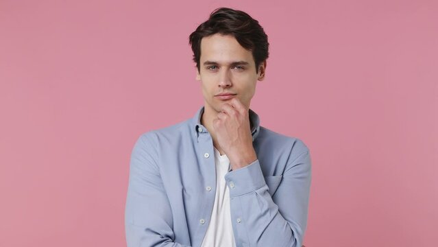 Fun insighted smart proactive pensive young brunet man 20s wears blue shirt looks around thinks scratches at temple comes up with ideas raised finger isolated on plain pink background studio portrait