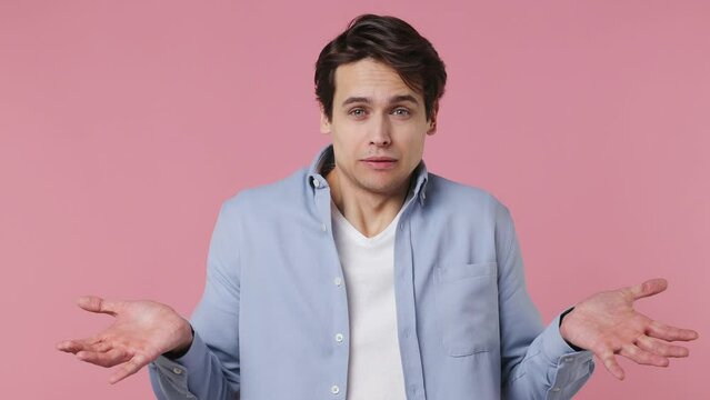 Fun confused shy shamed magnificent young brunet man 20s years old wears blue shirt looking camera spreading hands say oops ouch oh omg i am so sorry isolated on plain pink background studio portrait