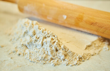 Grey flour and a rolling pin for dough. Raw products for the preparation of flour products. Organic food.