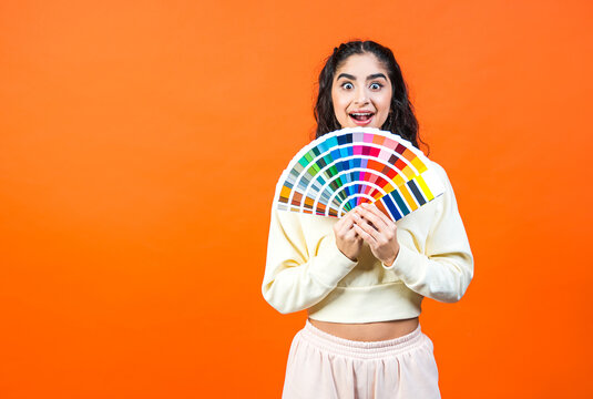 Beautiful surprised woman with color palette fun. Paint and painting concept. Interior designer woman holding color palette guide on orange background with copy space.