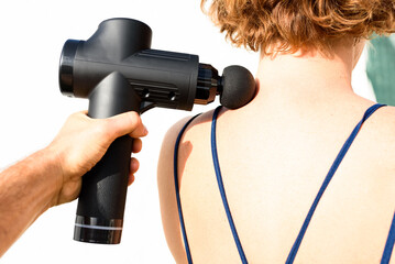 Back pain treated with a percussive self-massage gun in a mature woman.