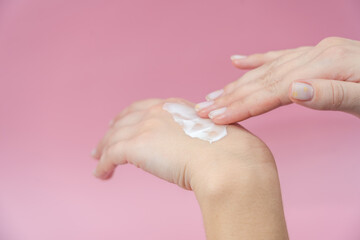 Naklejka premium Female hands rubbing the cream on pink background. Skincare, Spa salon