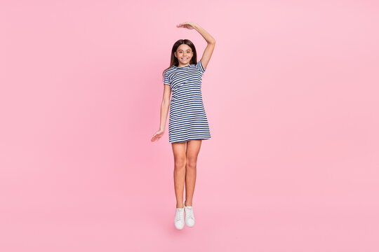 Photo of cute charming girl wear striped dress jumping high measuring height isolated pink color background