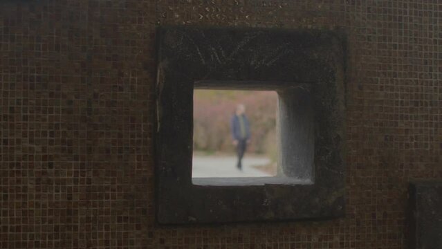 Hidden surveillance of a criminal through a square hole in the street wall. The silhouette is out of focus, a car drives by. Unrecognizable person.