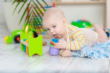 baby boy licking or nibbling toys in the children's room, cute little baby playing on the floor, children's development and play concept