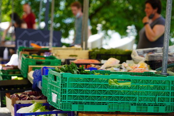 Market stall with vegetables and fruits. There are defocused persons on the background. The different types of vegetables are in green plastic crates. 