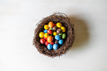 Chocolate eggs in a nest on a white wooden background.