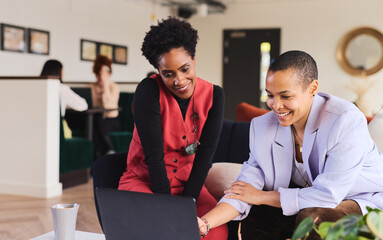 Mixed race LGBTQ mid adult woman and mature black woman using laptop
