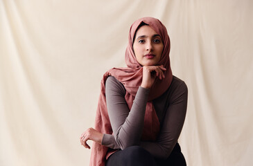 Portrait of confident young Middle Eastern woman wearing hajib looking at camera with hand on chin