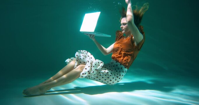 Beautiful young happy business woman in casual office clothes dives under water to use laptop and work slow motion.