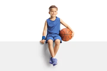 Fotobehang Smiling boy in a jersey holding a basketball and sitting on a blank panel © Ljupco Smokovski