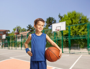 Boy in a blue jersey holding a basketball on a basketball court