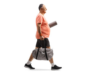 Naklejka premium Full length profile shot of a mature man in sportswear walking with a sports bag and exercise mat