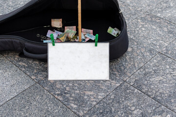 Open case for street musician guitar with banknotes and coins inside and with blank sign in...
