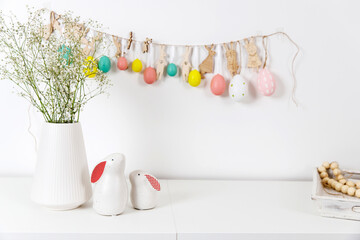 Fragment of the interior. Decorated children's room for Easter. A garland of plastic eggs on the wall. Ceramic rabbits and wooden cubes on the table. Place for your text. Easter card.