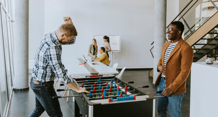 Young casual multiethnic business people playing table football and relaxing at office