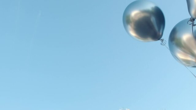 Silver helium balloons fly down attached to grey box hitting on surface of ground. Airdrop of inflatable balls against blue sky super slow motion