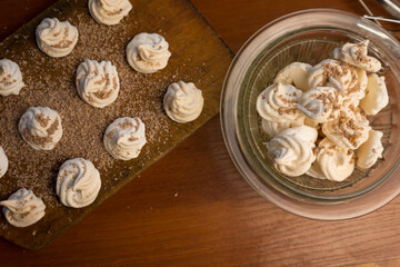Delicious crispy homemade egg meringue sprinkled with grated dark chocolate, prepared with love on a wooden background, crunchy dessert for coffee or tea.
