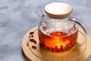 Glass teapot with hot tea with goji berries on a bamboo stand. Selective focus.