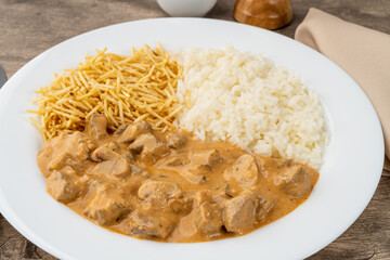 Meat strogonoff with rice and straw potato over wooden table