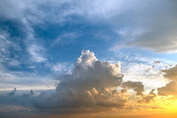 Dramatic moody sunset landscape with puffy clouds lit by yellow setting sun and blue sky
