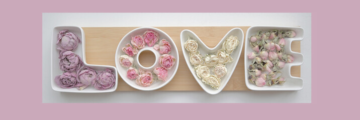 Valentine's day and love concept. The word love is made up of white porcelain molds filled with rosebuds against a soft delicate pink background.