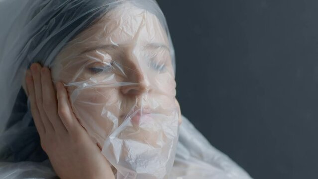 A blonde teen girl breathes through polyethylene and suffocates, cannot breathe through a bag, close up, hand on face