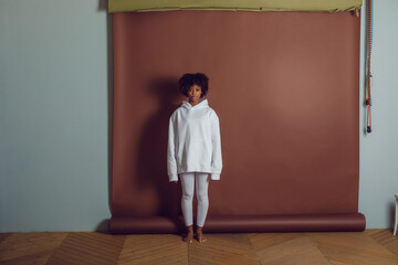 African american woman in a white hoodie and leggings stands on a brown background. Mock-up.