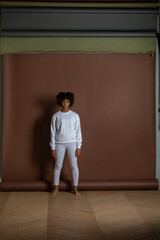 African-American girl in a white sweatshirt and leggings stands on a brown background. Mock-up.