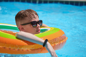 Portrait of happy child boy relaxing in inflatable circle in swimming pool on sunny summer day during tropical vacations. Summertime activities concept