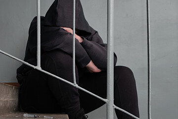 Depressed  teenage sitting alone after using drugs over grunge concrete wall. Drugs addiction. The...
