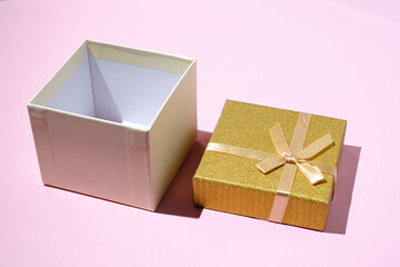 Blank open gift box or present box with golden ribbon bow on light pink pastel color background with shadow.