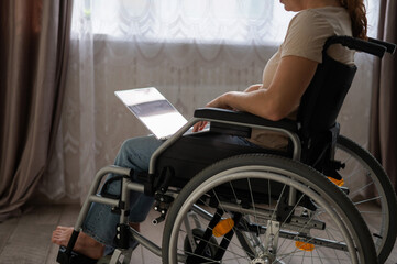 Obraz premium Caucasian woman in a wheelchair typing with a laptop from home. Remote work for people with disabilities.