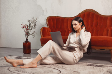 Young woman in cashmere clothes relaxing with laptop sitting at home on floor at couch