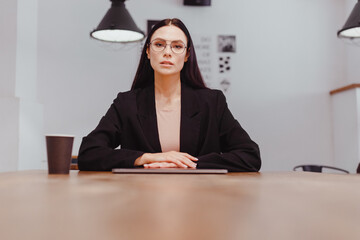 portrait of serious dissatisfied lady boss with stern look sitting at negotiating table - obrazy, fototapety, plakaty