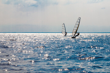 Two men on a horizon on a water sailing windsurfing board.
