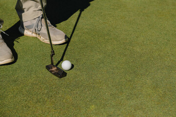 Details of the feet of a male golfer playing about to swing the ball on the green grass.