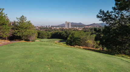 Golf course landscape with short green grass, some hills and trees.
