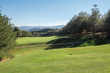 Fototapeta na wymiar Golf course landscape with short green grass, some hills and trees. 