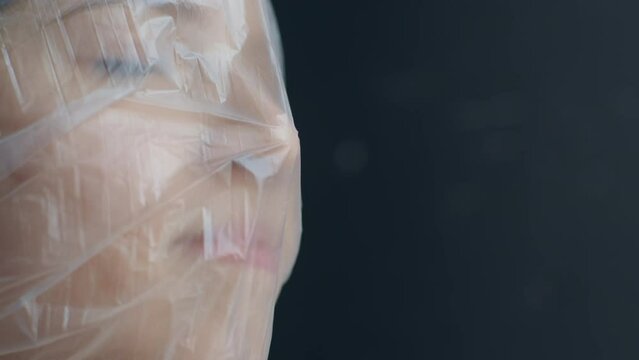 A blonde teen girl breathes through polyethylene and suffocates, cannot breathe through a bag, close up