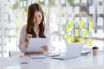 A beautiful Asian businesswoman sitting in her private office, she is checking company financial documents, she is a female executive of a startup company. Concept of financial management.