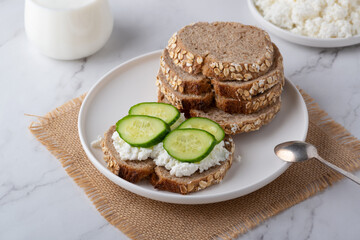 Slices of rye bread with cottage cheese and cucumbers on white background